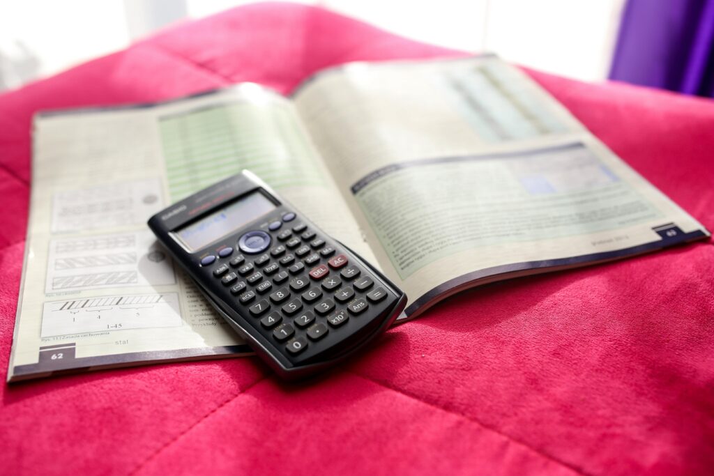 A scientific calculator and open textbook on a vibrant pink surface, ideal for education and academic themes.